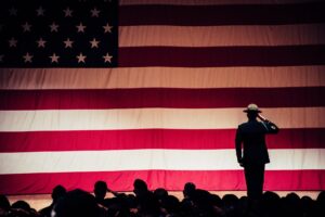 Silhouette of crowd of seated soldiers and one standing soldier saluting the American flag